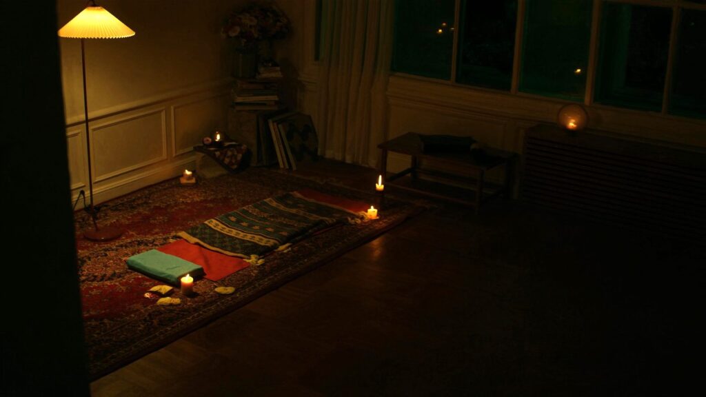 Stanza in penombra con tappetino, coperte e candele preparata per una pratica di Yoga Nidra